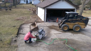 Next, Dennis unloads his bobcat and connects the hose to his concrete saw. The area of concrete just beyond him is what will be removed. 